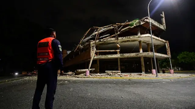 A Venezuelan municipal police officer stands next to a collapsed building in Valencia
