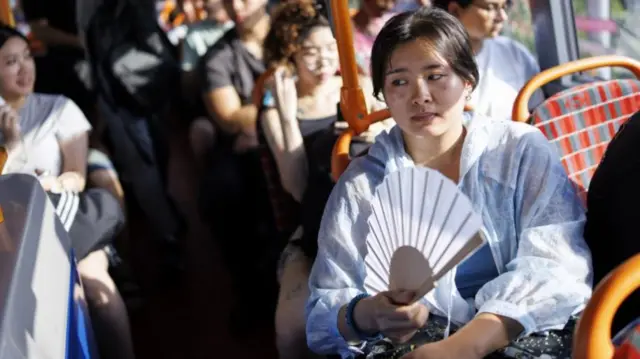 A woman uses a fan to cool down on a London bus service.