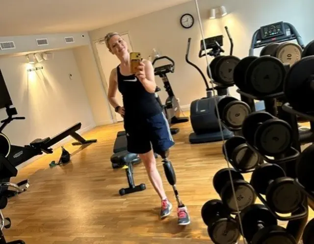 Sally Hurst poses in front of a mirror in a gym. She has a prosthetic leg, her left.