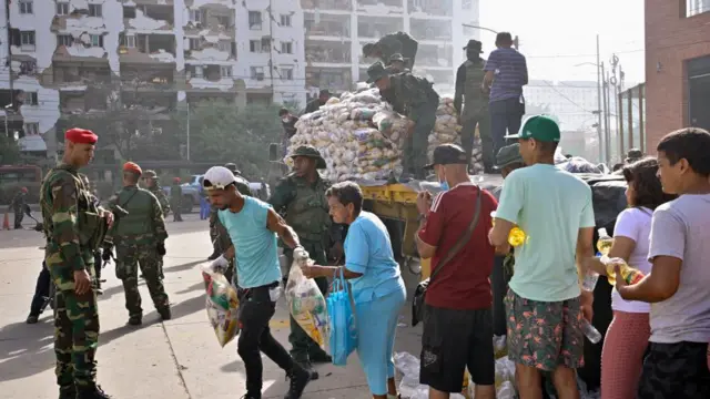 People collecting aid from a big truck, with military personnel standing guard