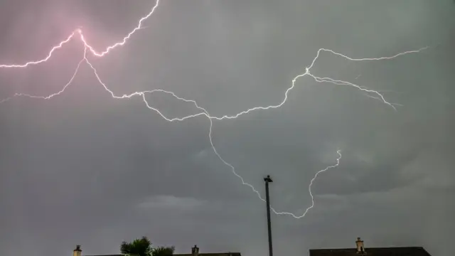 Lightning in a cloudy, night sky over houses