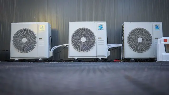 A row of three white air conditioning units lined up against a grey wall