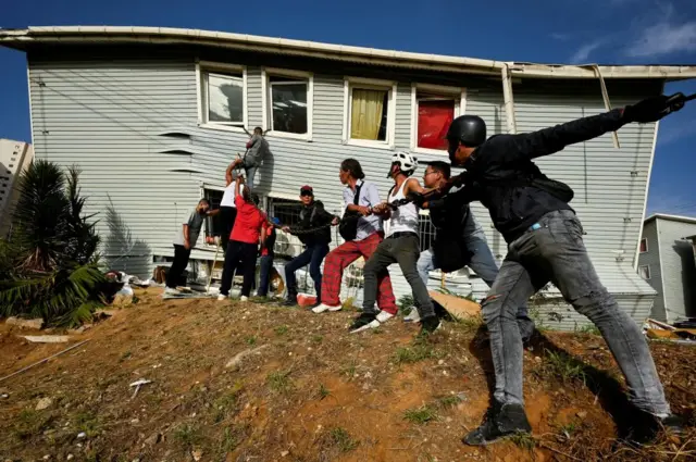 People assist in taking down a wall during rescue efforts in La Guaira