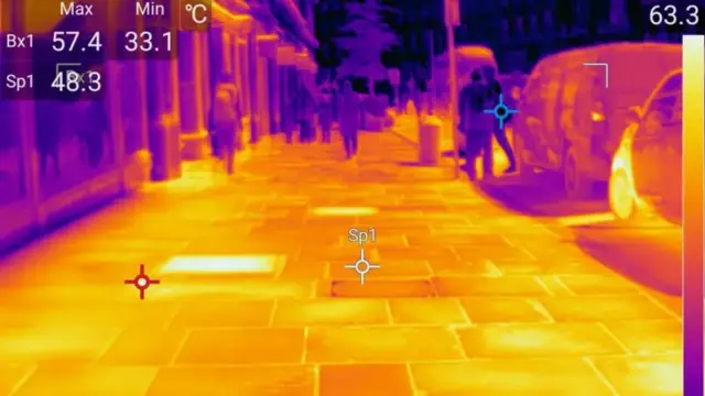 Thermal imaging photo showing a bright yellow pavement with darker, cooler figures walking along