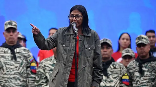 Delcy Rodríguez speaking into a microphone with men in military clothing behind her