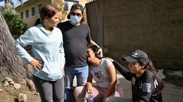 Three people comfort a fourth woman who is crying, she leans against a man for support