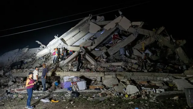 People stand next to - and on - the remains of a destroyed building