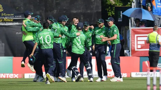 Ireland's players, wearing dark blue caps, green Ireland shirts, and dark blue trousers, embrace in celebration