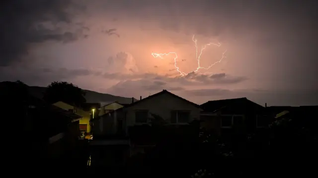 Bolt of lightning seen in the sky above some houses in the dark