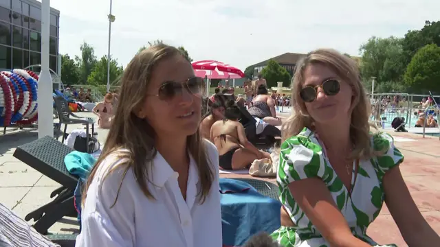 Two women wearing sunglasses sitting by the side of Hillingdon lido