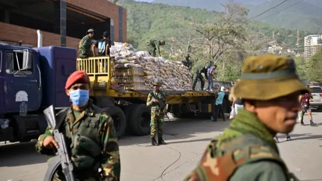 Military members seen outside a truck filled with white packages of aid
