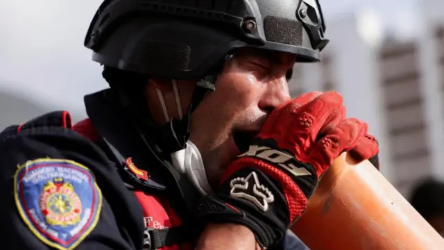 A firefighter wearing a helmet and protective gloves shouts into an orange tube