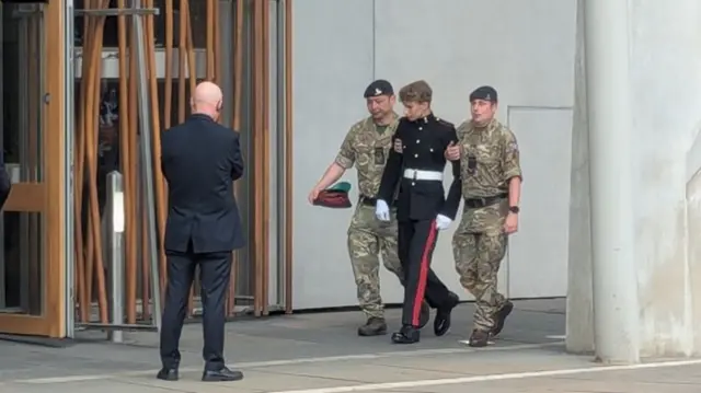 A soldier is helped into Holyrood