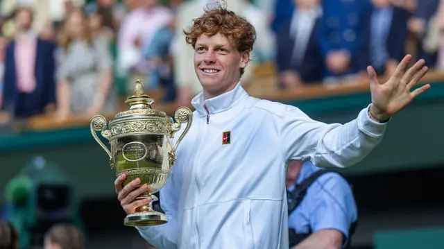 Jannik Sinner hold Wimbledon trophy and waves on court