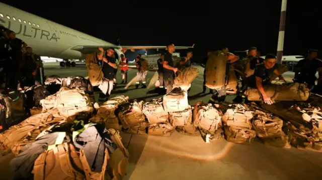 Bags of equipment and supplies are prepared by troops on the tarmac outside of a plane