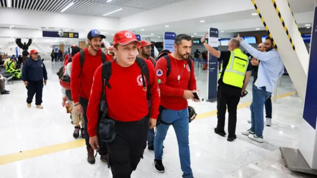 A group of people in red sweatshirts and caps walk through an airport