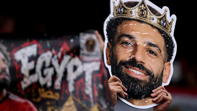 A fan holds up a picture of Mo Salah with a crown infront of an Egypt banner