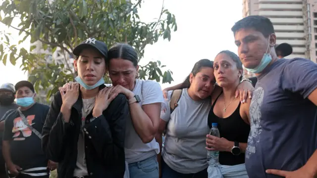 A group of five people embrace each other looking tearful