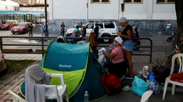 Women sort through their possessions outside a green tent on the streets of Caracas