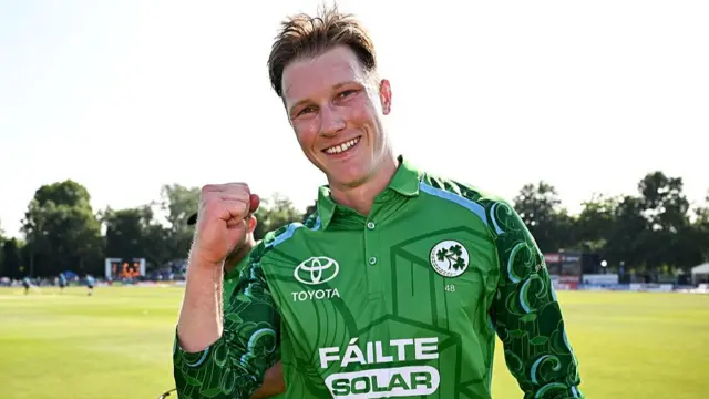 A smiling Harry Tector, wearing a long-sleeved green Ireland shirt, raises a clenched right fist
