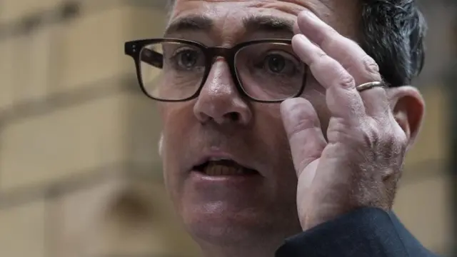 A close up picture shows Andy Burnham holding his glasses during his speech