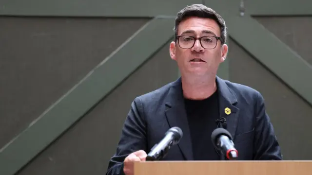 Andy Burnham speaks in front of two microphones