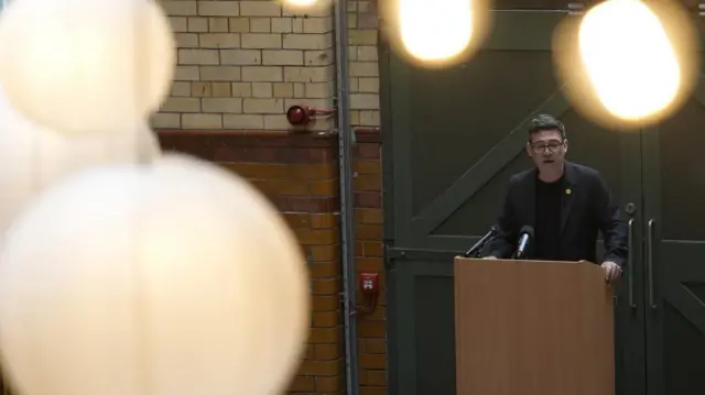 Andy Burnham delivers a speech at the People's History Museum. Several lights can be seen in front of Burnham as he delivers his speech