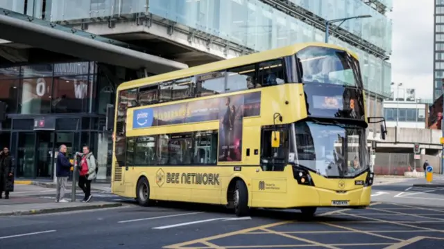 A yellow double decker bus turning a corner on an empty road. Two men wait on the corner