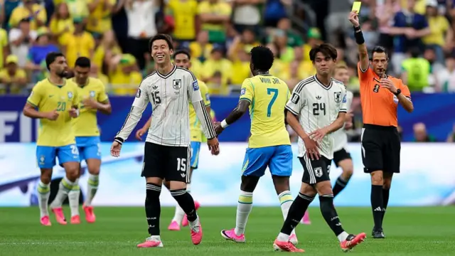 Referee Maurizio Mariani issues a yellow card to Daichi Kamada #15 of Japan during the FIFA World Cup 2026 Round Of 32 match between Brazil and Japan.