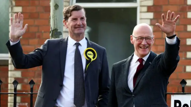 SNP Westminster leader Dave Doogan with SNP leader John Swinney. Two men wearing suits, waving while at a polling station.