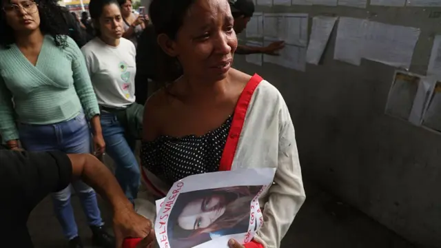A shows a picture of a missing person and looks visibly upset, while behind her a man searches a wall with information posted on it