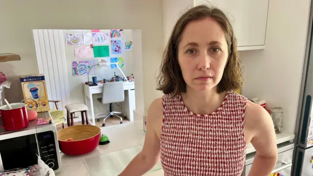 A woman in a red and white chequered dress stands in a kitchen