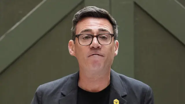 Andy Burnham speaks during a speech in Manchester. He is wearing a suit with a yellow badge with a bee on it