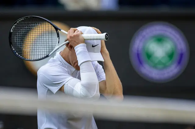 Jannik Sinner holds his head and has a tennis racquet in his hands