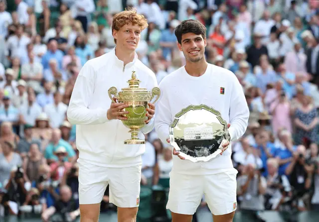 Jannik Sinner holds the Wimbledon title and stands next to Carlos Alcaraz who has the runners-up plate