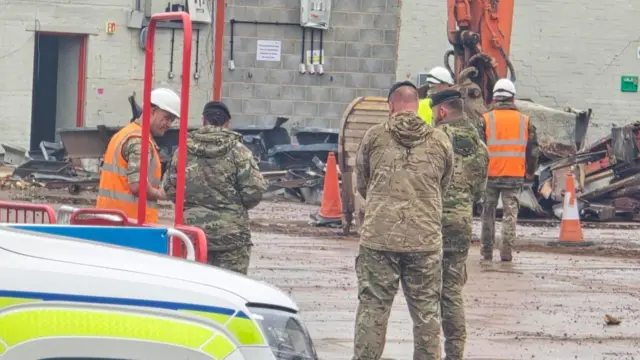 At least five people in Army uniform, with a building in the background.