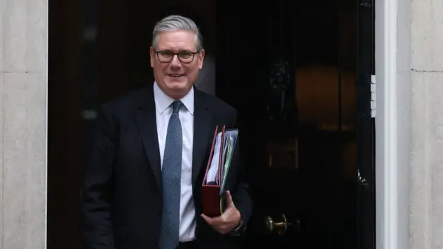 Starmer smiles as he walks out of No 10 holding two binders