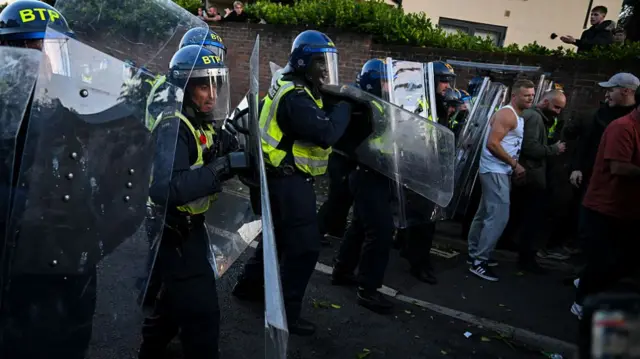 Police hold shields with a line of protesters in front of them