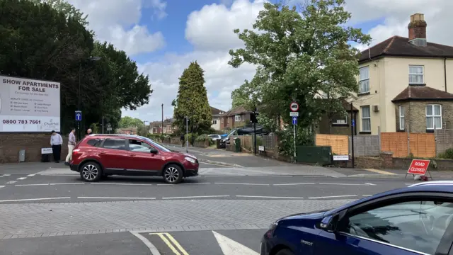 A street scene with two parked cars and houses lining the road