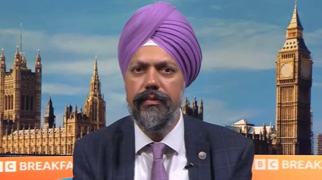 Tan Dhesi speaks on BBC Breakfast. He is wearing a purple turban and a matching purple tie with a suit. A BBC Breakfast backdrop with a picture of Westminster can be seen in the background