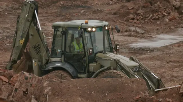 An Army digger can be seen at the site surrounded by dirt and rubble