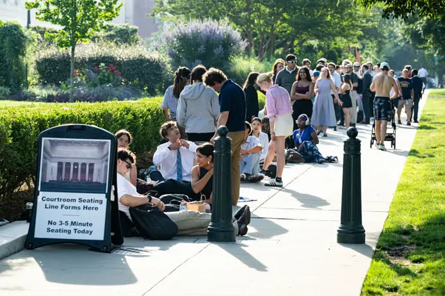 People sit in a line on the sidewalk outside the Supreme Court