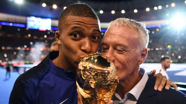 Kylian Mbappe and Didier Deschamps kiss the World Cup trophy