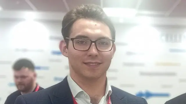 Oliver Tatlow - a man wearing a blazer and shirt, and glasses.