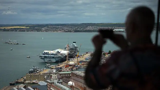 The silhouette of a man can be seen taking a picture of the HMS Queen Elizabeth aircraft carrier in Portsmouth