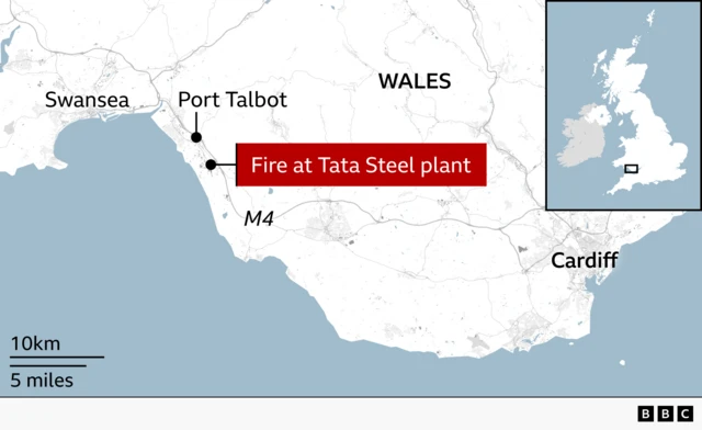 Map of south Wales showing the location of a fire at the Tata Steel plant in Port Talbot, marked by a red callout box and dot along the coast between Swansea and Cardiff. Nearby places including Swansea, Port Talbot, Cardiff, and the M4 motorway are labelled, with an inset map of the UK highlighting the area.