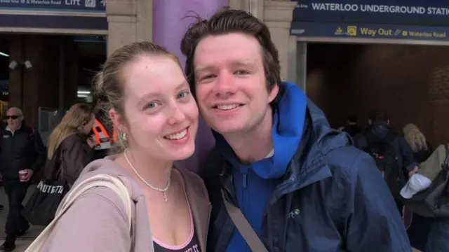 Eve Osborne and Ed Bond are pictured at Waterloo Station. They are a young couple wearing hoodies and carry shoulder bags.