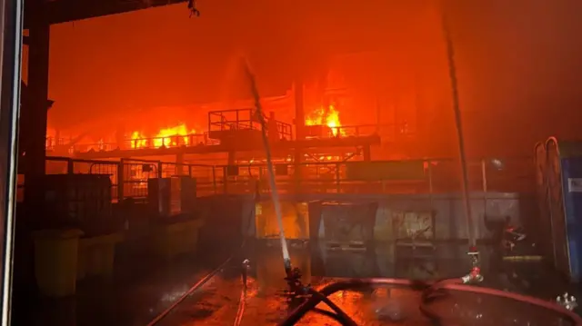 Red flames pictured at Tata Steel plant in Port Talbot with hose directed towards flames in attempt to contain blaze