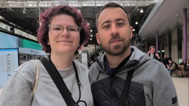 Cinna and Stephan are pictured at Waterloo station wearing a hoodie and sweatshirt, they are both smiling.