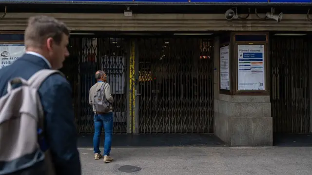 A man wearing a backpack stands outside the closed barrier gates at Holborn station